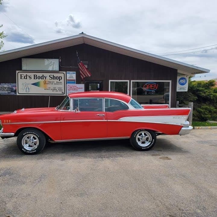 Red and white 1957 Chevrolet parked in front of Eds Body Shop storefront